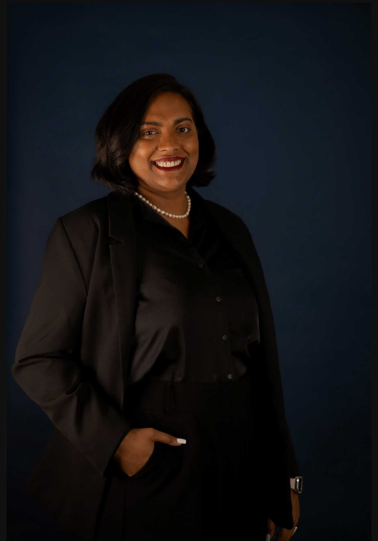 Portrait of Attorney Nisha Williams, smiling and wearing a black suit against a dark blue background.